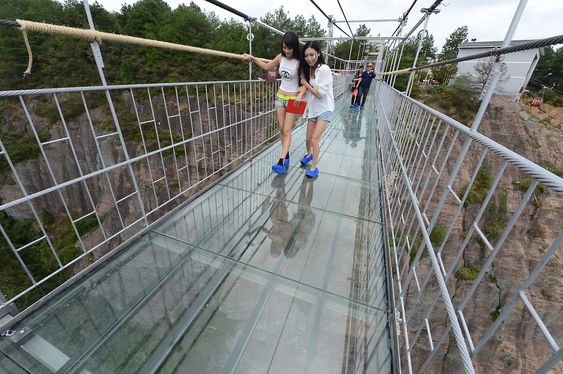 PINGJIANG, CHINA - SEPTEMBER 24: (CHINA OUT) Tourists walk on a suspension bridge made of glass at the Shiniuzhai National Geological Park on September 24, 2015 in Pingjiang County, China. The 300-meter-long glass suspension bridge, with a maximum height of 180 meters, opened to the public on Thursday. (Photo by ChinaFotoPress/ChinaFotoPress via Getty Images)
