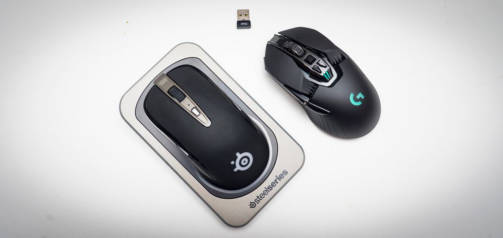 SteelSeries Sensei Wireless (t.v.) med sin basestasjon som også fungerer som musens trådløse tilkobliingspunkt, og Logitech G900 (t.h.) med sitt mye mindre, trådløse tilkoblingspunkt. Den ene er litt enklere å ta med seg enn den andre.