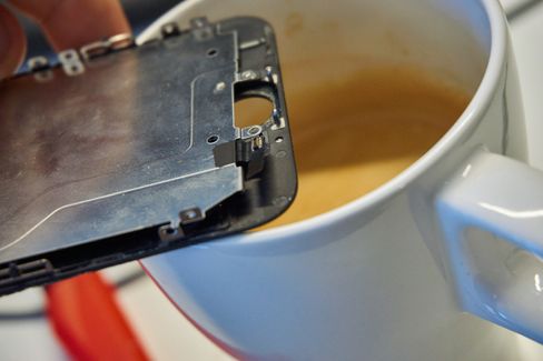 17. Vi hadde ingen varmepistol for hånden, men ved å holde skjermen inntil en varm kopp kaffe fikk vi løsnet limet på kabelen til hjemknappen. Vi gjorde IKKE som på bildet – det er kun en illustrasjon, og er både ineffektivt og utsetter delene for fuktighet!