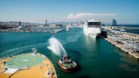 Taubåter hilser det nye cruiseskipet med å sende kaskader av vann opp i lufta ved avgang fra Barcelona.