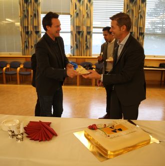 Administrerende direktør Nils Morten Huseby (t.h.) serverer atommerket kake til daglig leder Nils Bøhmer i Bellona for å feire at Venstre (representert med Abid Q. Raja i bakgrunnen) økte bevilgningene til Ifes atomopprydding med 20 millioner kroner i budsjettforliket.