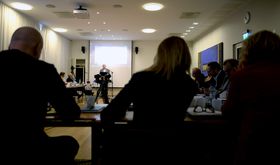 Sven Egil Omdal (i bakgrunnen) talte for Kringkastingsrådet for noen uker siden. Nærmest kamera, fra venstre og med ryggen til: NRK-sjef Thor Gjermund Eriksen, nyhetsdirektør Alexandra Beverfjord og distriktsdirektør Grethe Gynnild-Johnsen.
