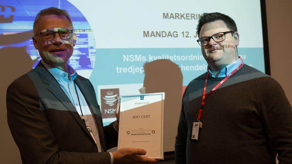 NSM-direktør (fra v.) Kjetil Nilsen overrekker beviset på at BDO oppfyller kravene til kvalitetsordningen for hendelseshåndtering til Chris Culina.