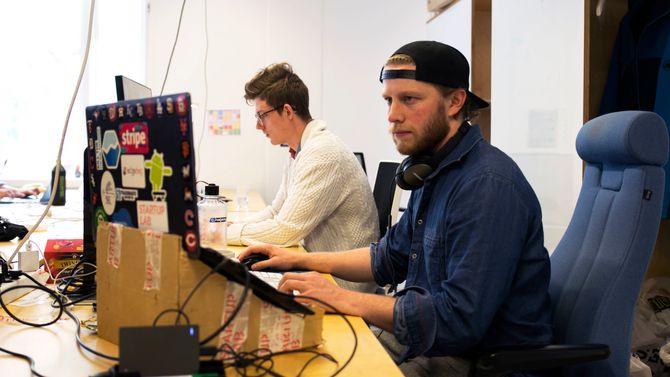 «Jeg brukte tid på å lene meg ned for å se på laptopen, så jeg lagde en slags forhøyet dockingstasjon av papp. Den funker fjell!». I bakgrunnen sitter administrerende direktør i det lille selskapet, Marius Norheim.