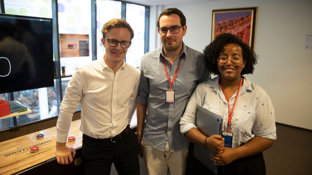 Får skryt for en god leveranse: (Fra v.) Sondre Brekke, Niklas Johansen og Siddise Hirpa. Summer internship i halvannen måned har ikke bare vært alvor, men også lek og moro. Bak ser vi deler av en poengteller for shuffleboard. Maskinlæring inngår også i den løsningen, som holder oversikt over hvor de røde og blå puckene befinner seg på spillbrettet.