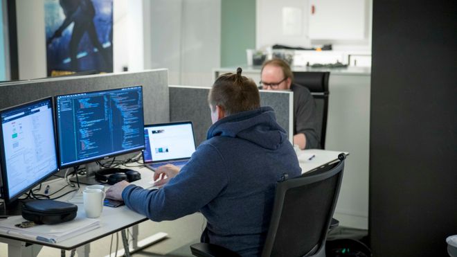 To utviklere sitter foran skjermer og programmerer.