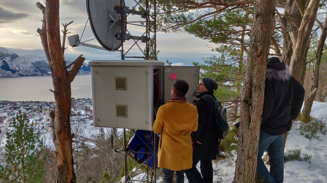 Tre personer i ved parabolantenne og stor boks som inneholder utstyr for videreformidling av signaler via 4G eller 5G.