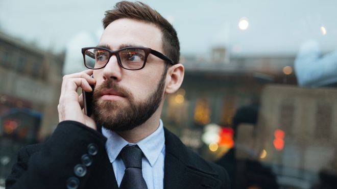 Pent kledd mann snakker i mobiltelefon utendørs.