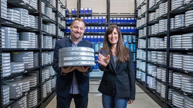 Brad Collar, sjef for globale arkiver og medieteknikk hos Warner Bros., holder fire filmruller med filmen «Superman» fra 1978, mens Vicky Colf, teknologidirektør i Warner Bros. holder en liten glassplate som i alle fall kan lagre innholdet på 22 slike filmruller.