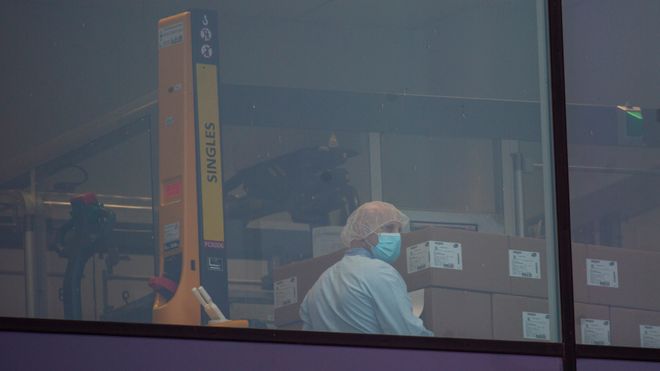 En ansatt i legemiddelfirmaet Pfizer, iført ansiktsmaske, som pakker esker ved en fabrikk i Belgia, torsdag 3. desember 2020.