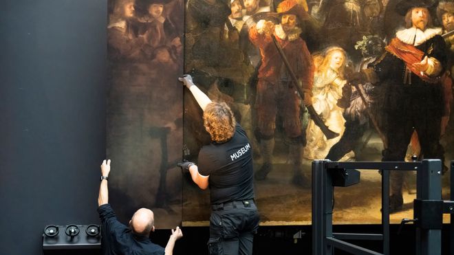 To museumsarbeidere henger opp en av de nye kantene til bildet Nattevakten av Rembrandt