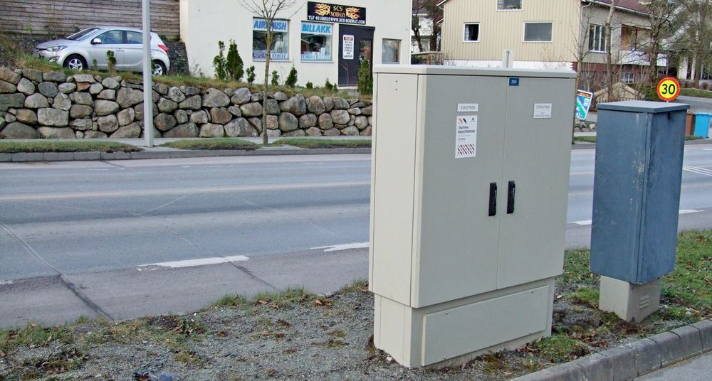 Nytt og gammelt telleskap. Det nye er egentlig to skap. Det ene er for sterkstrøm. Det kan bare autoriserte elektrikere åpne. Det andre er for svakstrøm. Det kan alle med nøkkel hente trafikkinformasjon fra. Sporene i asfalten er synlige til venstre på bildet. (Foto: )