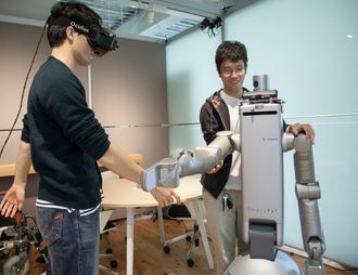 Masterstudenten Akio Shigekane og Yuta Watanabe, sammen med en robot som kan bidra innen pleie.