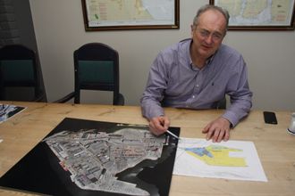 Einar Olsen med flyfoto av havna og tegning med planer for neste utfylling. Bukta på bildet skal fylles og øker arealet med 75.000 kvadratmeter.