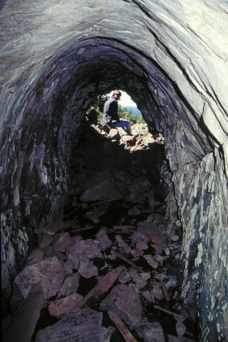 Vigsnes gamle gruve, med den vassfylte gruveopninga i framgrunnen, og bygget med Vigsnes Grubemuseum i bakgrunnen.