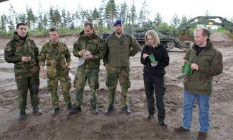 Tid for lunsj. Grenader Olsen (f.v.), Sersjant Strand og Fenrik Flatla spiser brødmat. Løytnant Jakobsen spiser nøtter (som han gjemmer på ryggen). Gina og Ernst Morten får prøve feltrasjoner, med en viss skepsis.