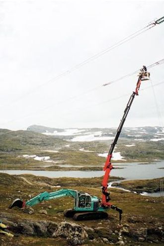 En av de første jobbene til Kobelco-maskinen var på Geitryggen mellom Hol og Aurland. Etter 2 timers belting inn på fjellet ble karene fra Hallingmast løftet opp i kurven for å skifte ut revolveringene (sløyfer) på en høyspentledning.
