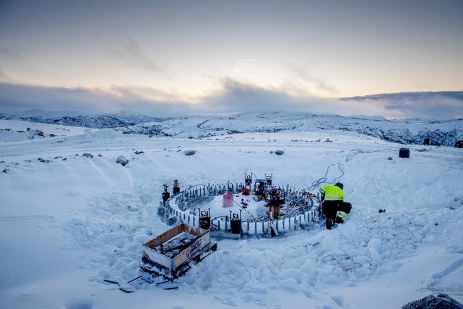 En elektriker arbeider med fundamentet til en vindturbin i Roan vindpark i desember. Fjelltoppen er dekket av snø.