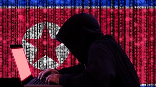 Mann i hettegenser sitter ved laptop foran nordkoreansk flagg.