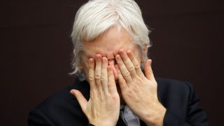 Julian Assange holder hendene foran ansiktet. 