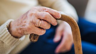 A close-up of a lonely senior woman sitting on an armchair at home, holding a walking stick.