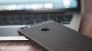 Iphone ligger på et bord delvis oppå en Macbook.
