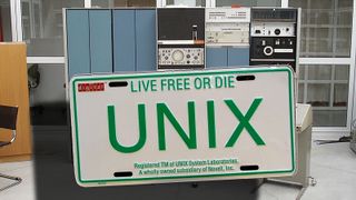 Bilskilt med teksten UNIX: Live free or die, foran et tilsvarende system som det Unix først ble utviklet for – DEC PDP-7 – fotografert ved Universitetet i Oslo i 2005.