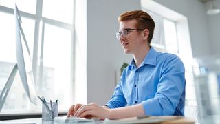 Ung mann som sitter ved et skrivebord og jobber med en PC.