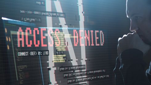 Hacker ved en PC med med "access denied"-melding på skjermen.