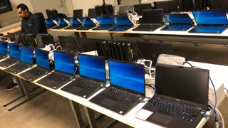Én mann arbeider på en laptop mens flere titalls flere maskiner står på rekke og rad og venter på å bli gjort klar.
