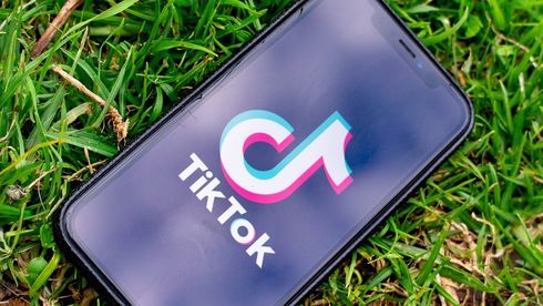 TikTok-logoen på en smartmobil som ligger på en gressplen.