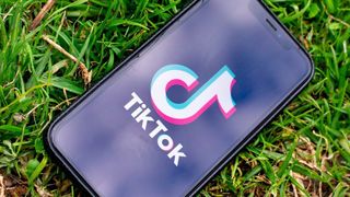 TikTok-logoen på en smartmobil som ligger på en gressplen.