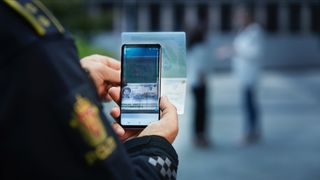 Armen til en person i politiuniform holder en telefon som tar bilde av et pass. 