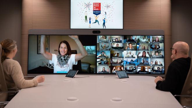 Ansatte i Cisco deltar med hvert sitt skjermbilde i et digitalt møte på en storskjerm på veggen, mens to personer deltar i samme møte fra et fysisk møterom.