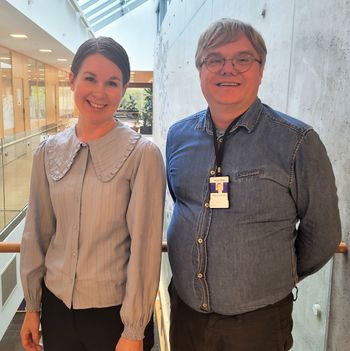 Portrettfoto av de to prosjektlederne smilende foran en grå murvegg