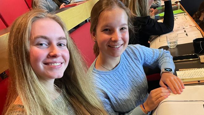 To smilende jenter i genser med A3-ark med tegning av tomme mobilskjermer