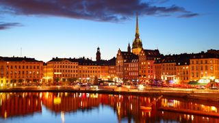 Illustrasjonsfoto: Stockholms gamleby i kveldslys. Bygningene i varmt lys speiler seg i vannet.