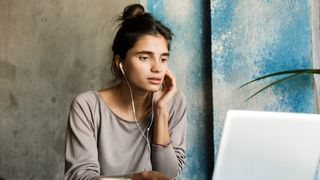 En ung kvinne sitter ved et bord og jobber på en laptop med en kaffekopp ved siden av seg