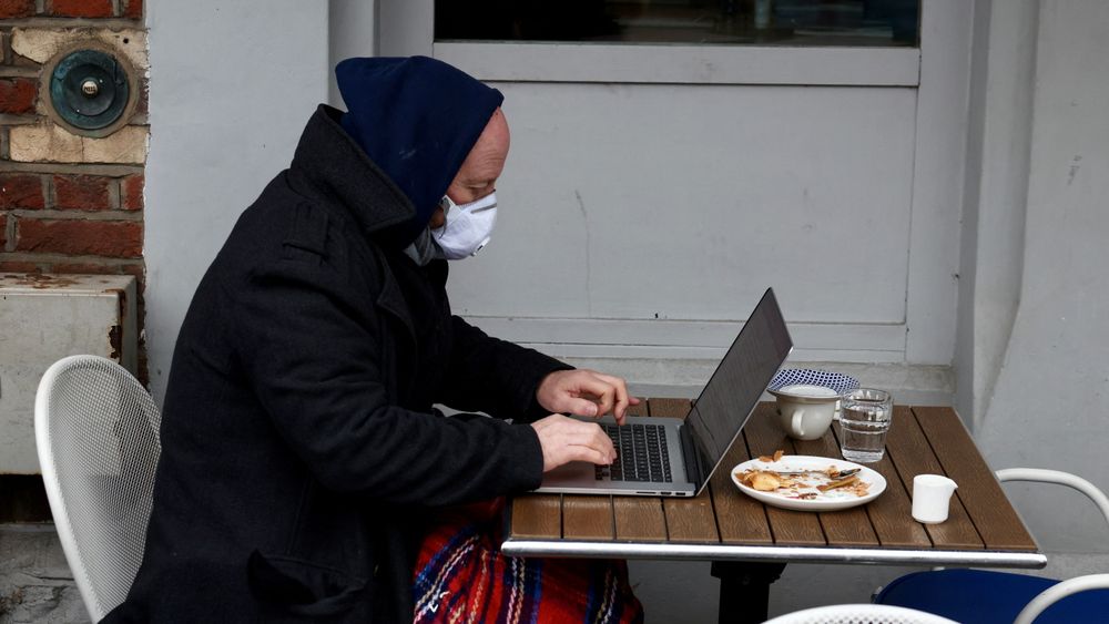 Fjernarbeid under koronapandemien bidrar til et PC-salg verden ikke har sett på ti år. Bildet viser en mann med ansiktsmaske som jobber fra en kafé i London, rett før julen 2021.
