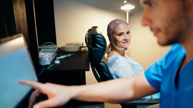 Pasient med EEG-måling på hodet, lege ser på dataskjerm.