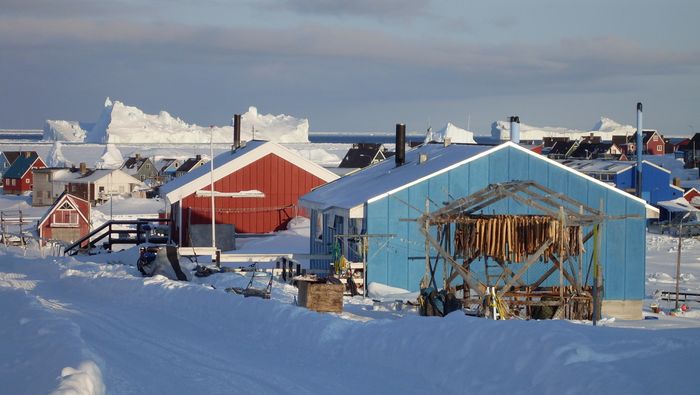 Grønland. bolighus i mange farger ved sjøen, isbreer i bakgrunnen.