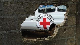Bil med logoen til International Committee of the Red Cross sett gjennom et hull i en murvegg.