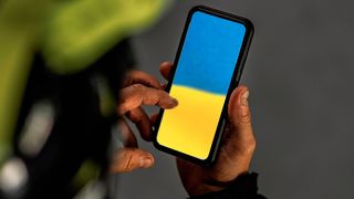 Mobiltelefon i hender, med fargene i det ukrainske flagget innmontert på skjermen.