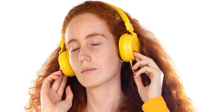 Rødhåret kvinne lytter til musikk med headset.
