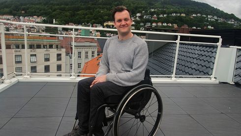 Ung mann i rullestol grå genser brunt hår på taket av bygning.  