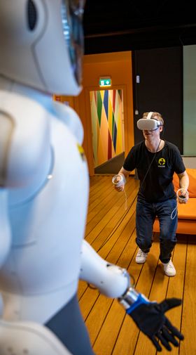 Bernt Børnich har tatt på seg VR-briller og kontrollere for å styre Eve til å bøye seg mot gulvet for å plukke opp ting. 