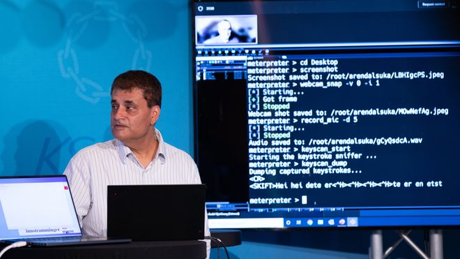 En mann står på en scene foran en skjerm som viser kode.