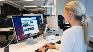 Kvinne sitter og jobber på pulten er en mac studio og en Mac studio Display skjerm