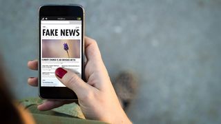 Kvinnehånd holder mobil med nyheter om fake news.