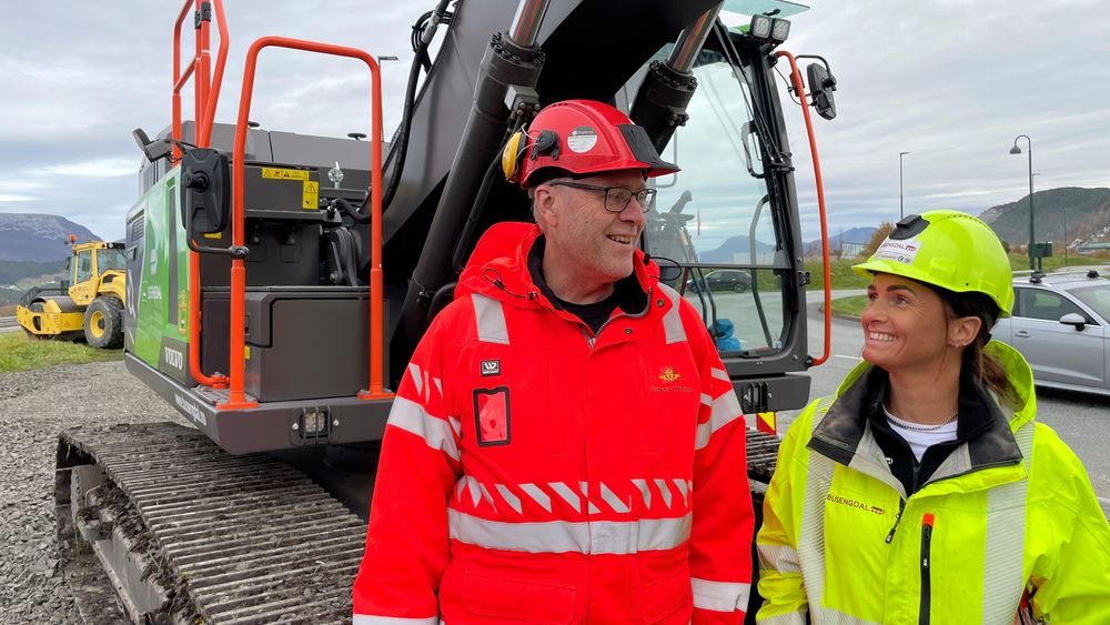 Ingar Valbø, byggeleder i Statens vegvesen og Kamilla Busengdal, prosjektleder i Busengdal foran Sunnmøres største elektriske gravemaskin.